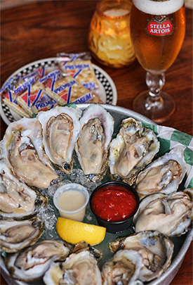 A plate of oysters with dipping sauce and two glasses.